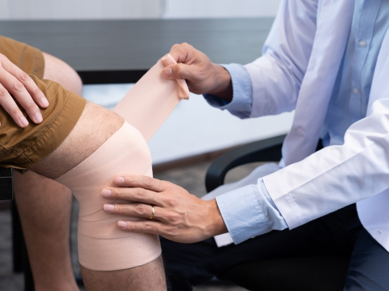 Elastik bandaj uygulayarak diz çevresindeki dokuları destekleyen doktor ve hasta